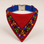 A red triangular dog bandana with colorful embroidered floral patterns along the border and a blue interior lining, shown on a light beige background.