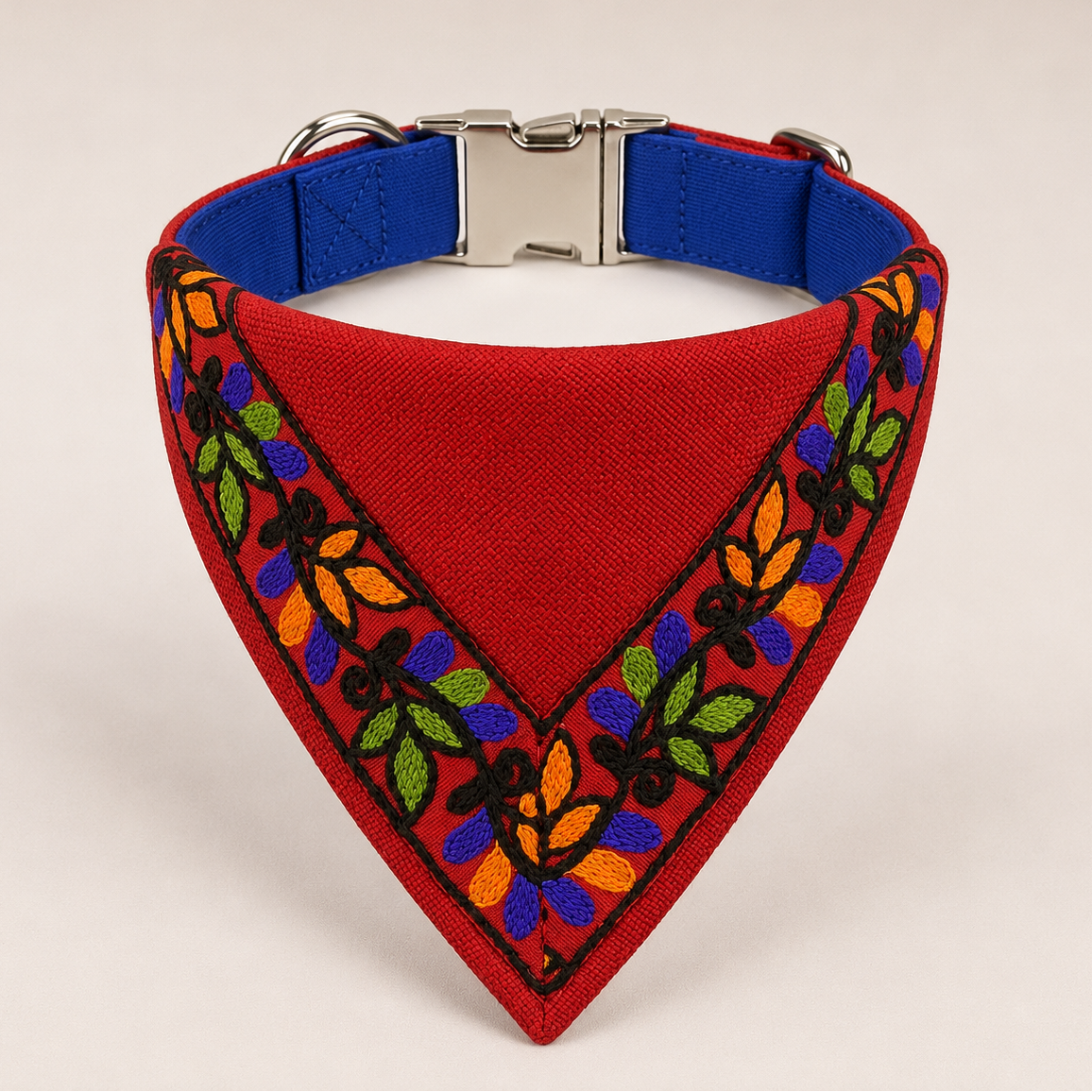 A red triangular dog bandana with colorful embroidered floral patterns along the border and a blue interior lining, shown on a light beige background.