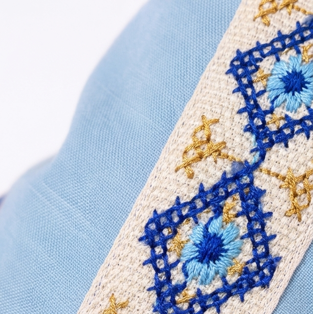 A close-up of a light blue fabric item featuring a decorative embroidered border with blue, beige, and gold geometric and floral patterns.