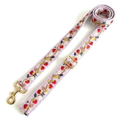 A light pink woven dog leash with an embroidered strawberry and leaf pattern, featuring gold-tone metal hardware including a swivel clasp and buckle, displayed on a white background.