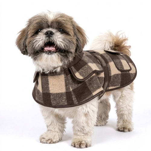 A small fluffy dog wearing a brown and beige plaid pet coat, standing against a solid white background.