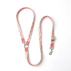 A fabric dog cross body leash with a red and white gingham pattern and a pink floral print, featuring silver metal hardware, laid out on a white background.
