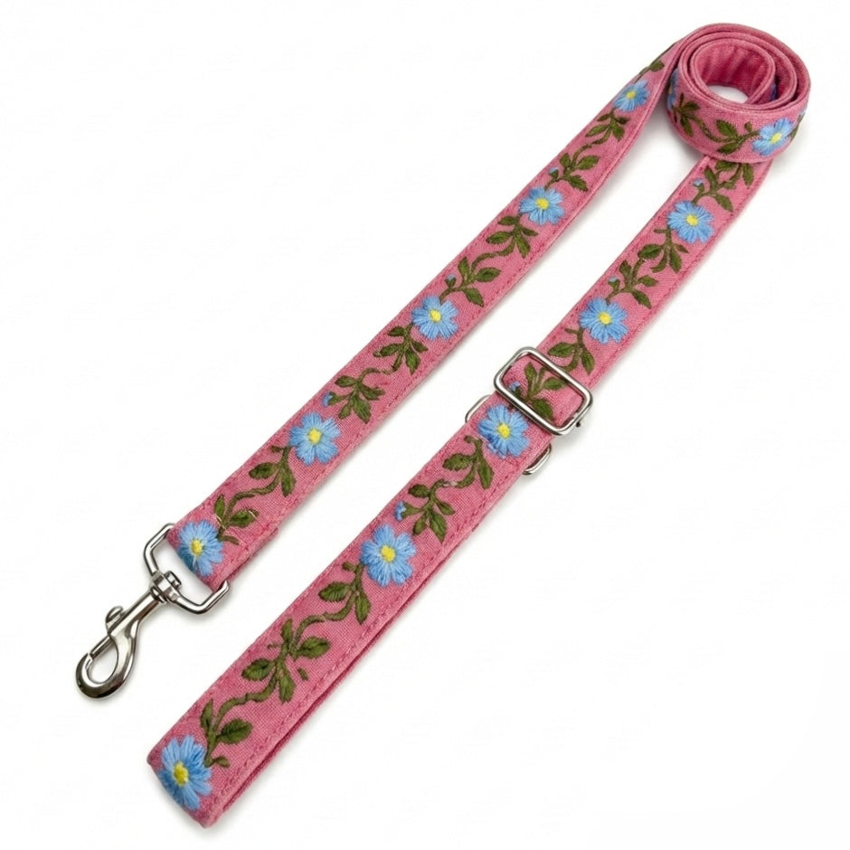 A pink fabric dog leash with an embroidered floral pattern of blue flowers and green leaves, featuring silver metal hardware including a swivel clasp and a quick-release buckle, shown on a plain white background.