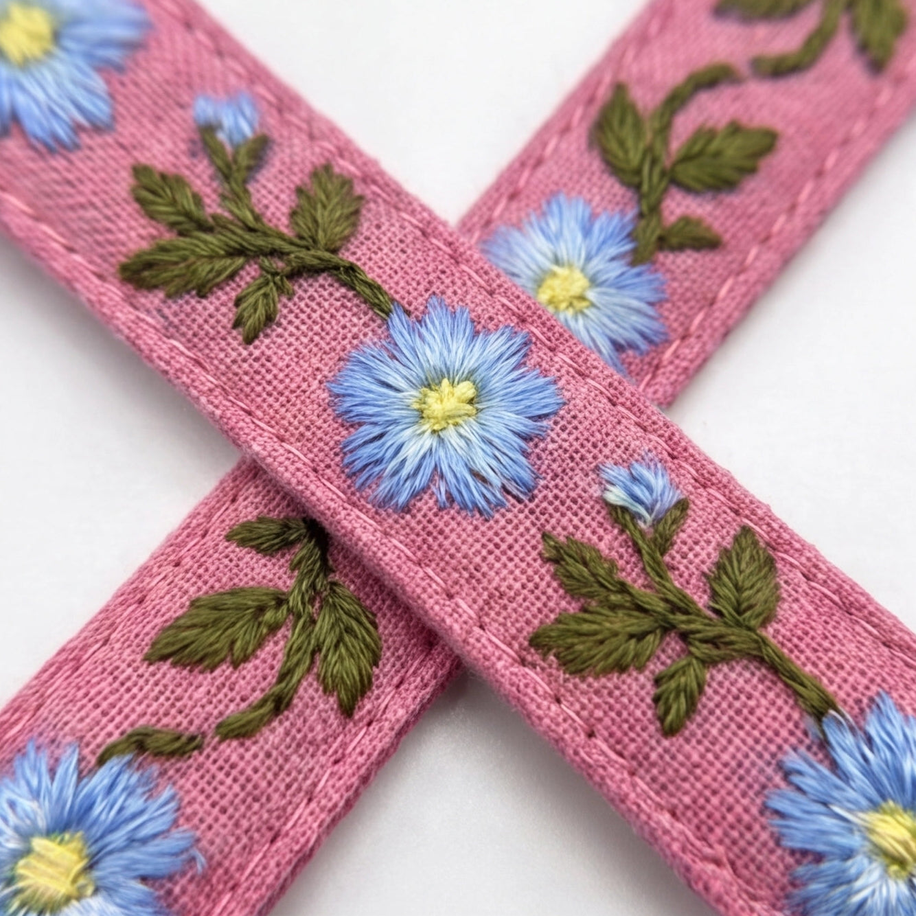 Pink fabric with blue floral embroidery on a white background