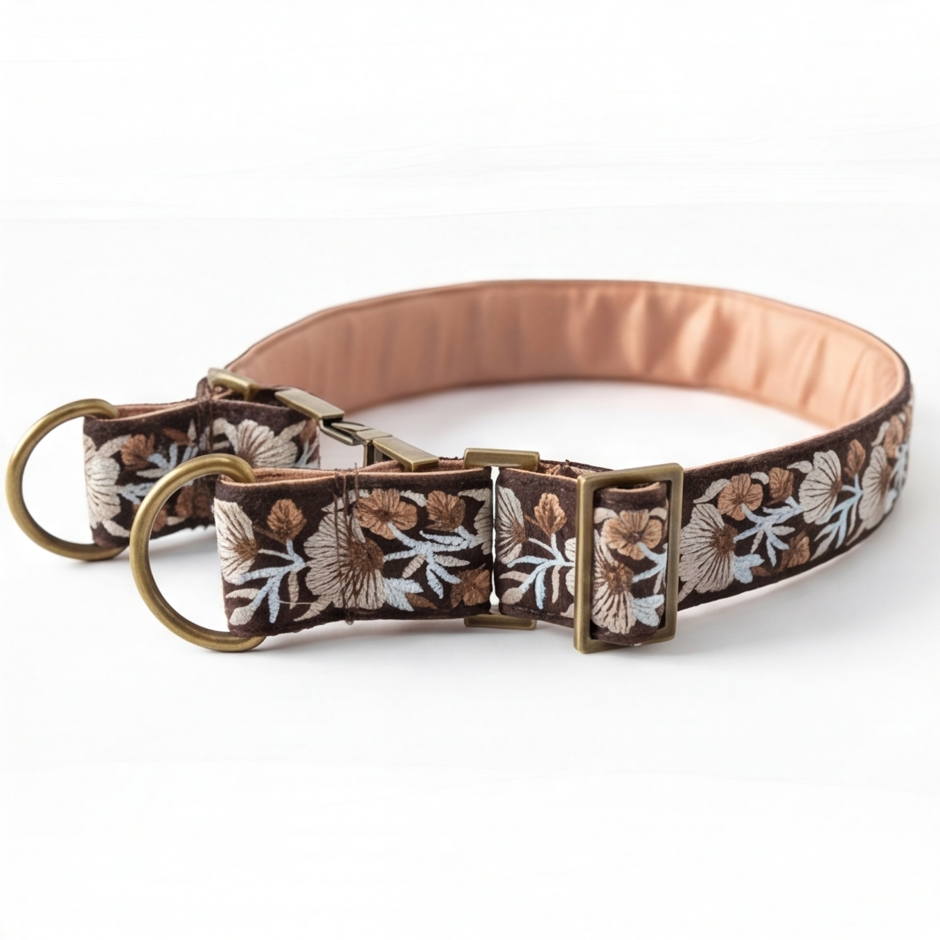 A brown fabric dog collar with an embroidered floral pattern in beige, white, and brown, featuring antique brass hardware, including a D-ring, buckle, and adjustment slider.