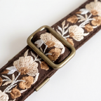 Floral embroidered belt with a brass buckle on a white background