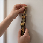 Hand holding a decorative brown leash with floral embroidered patterns against a neutral background