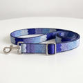 A woven fabric dog leash with a blue and purple gradient pattern, featuring a silver metal buckle and swivel clasp, displayed on a white surface.