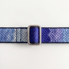 A close-up of a woven fabric strap with a blue and purple gradient pattern and a silver-toned metal buckle, shown against a plain white background.