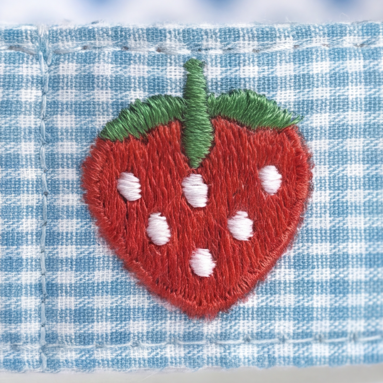 Embroidered strawberry patch on a blue checkered fabric background