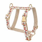 A dog harness with a beige and white gingham pattern, decorated with a red and blue berry vine print, and featuring gold-tone metal hardware.