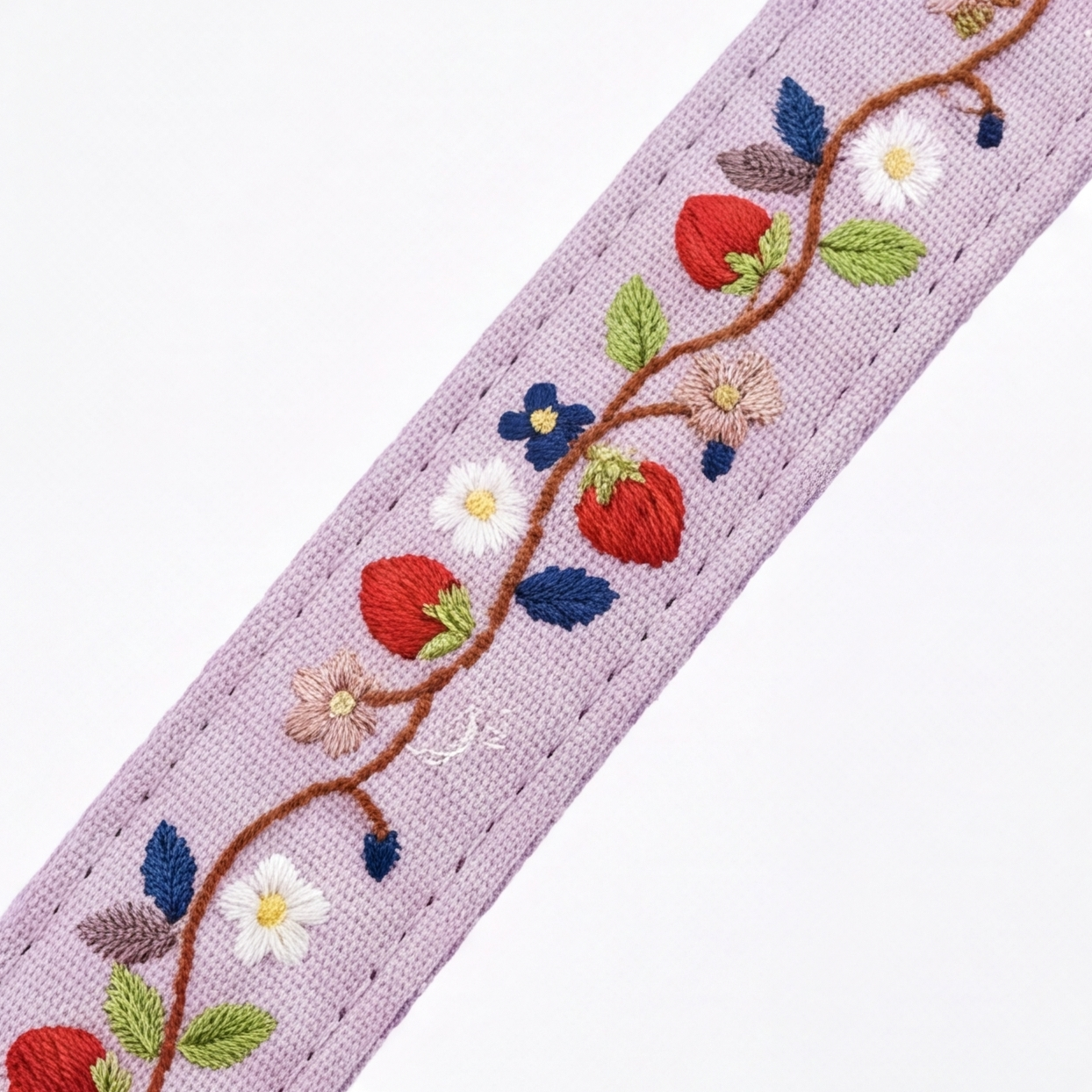 A close-up of a lavender embroidered fabric trim featuring a vine with red strawberries, white and blue flowers, green leaves, and small purple accents on a white background.