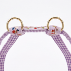 A close-up of a pet halter strap featuring a purple and white gingham pattern, embroidered floral details, and shiny gold metal rings on a white background.