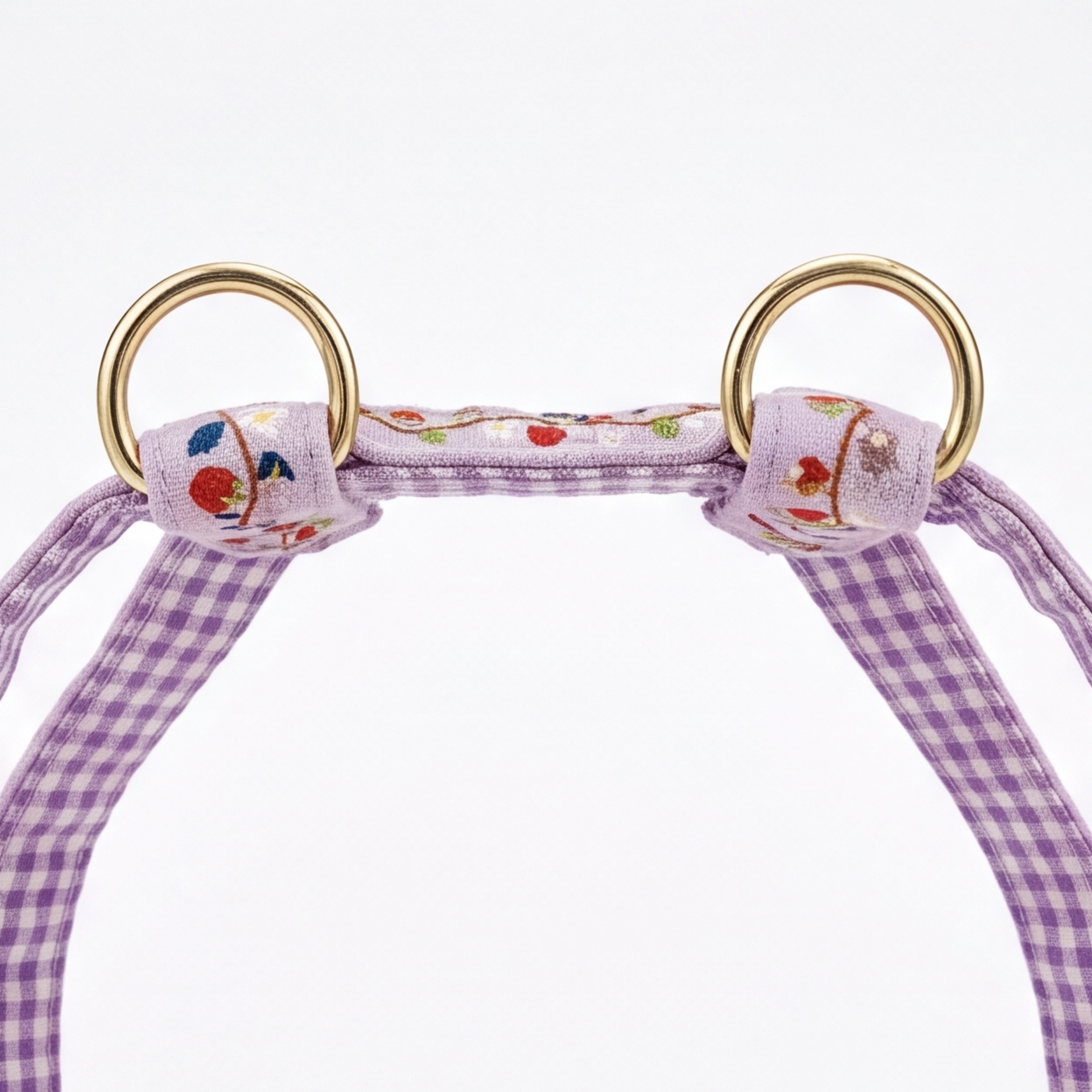 A close-up of a pet halter strap featuring a purple and white gingham pattern, embroidered floral details, and shiny gold metal rings on a white background.