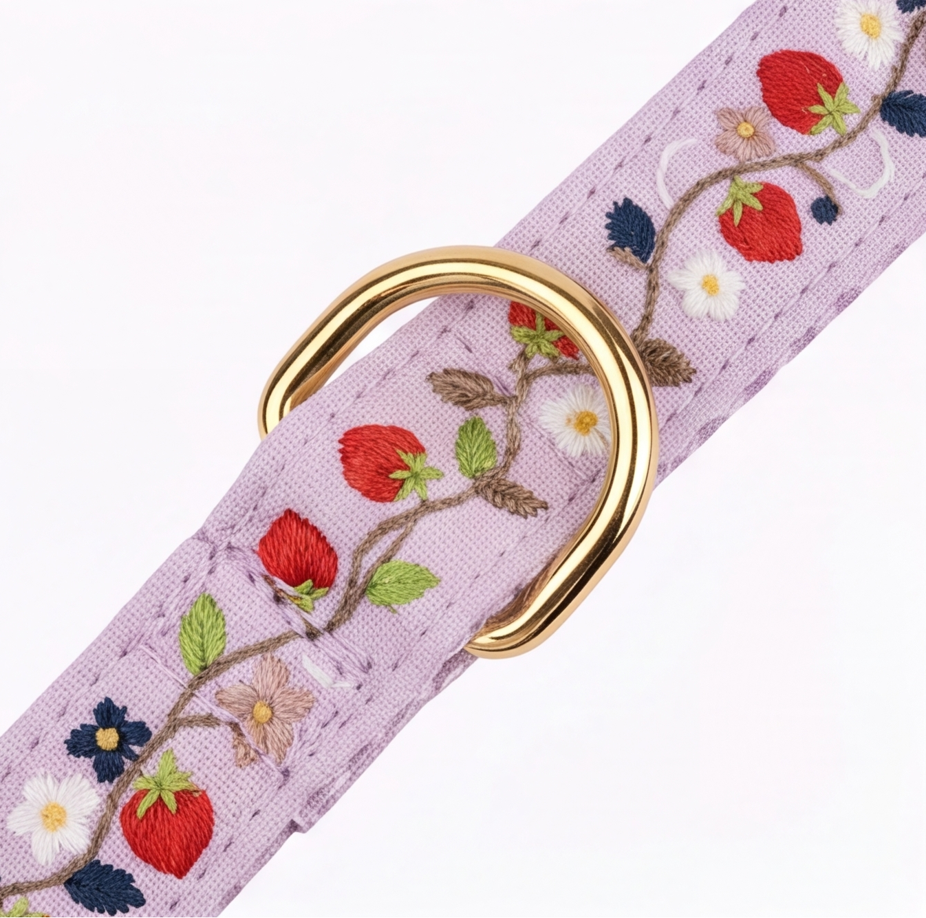 A close-up of a lavender woven strap with embroidered strawberries, flowers, and green leaves, featuring a polished gold metal D-ring clasp on a white background.
