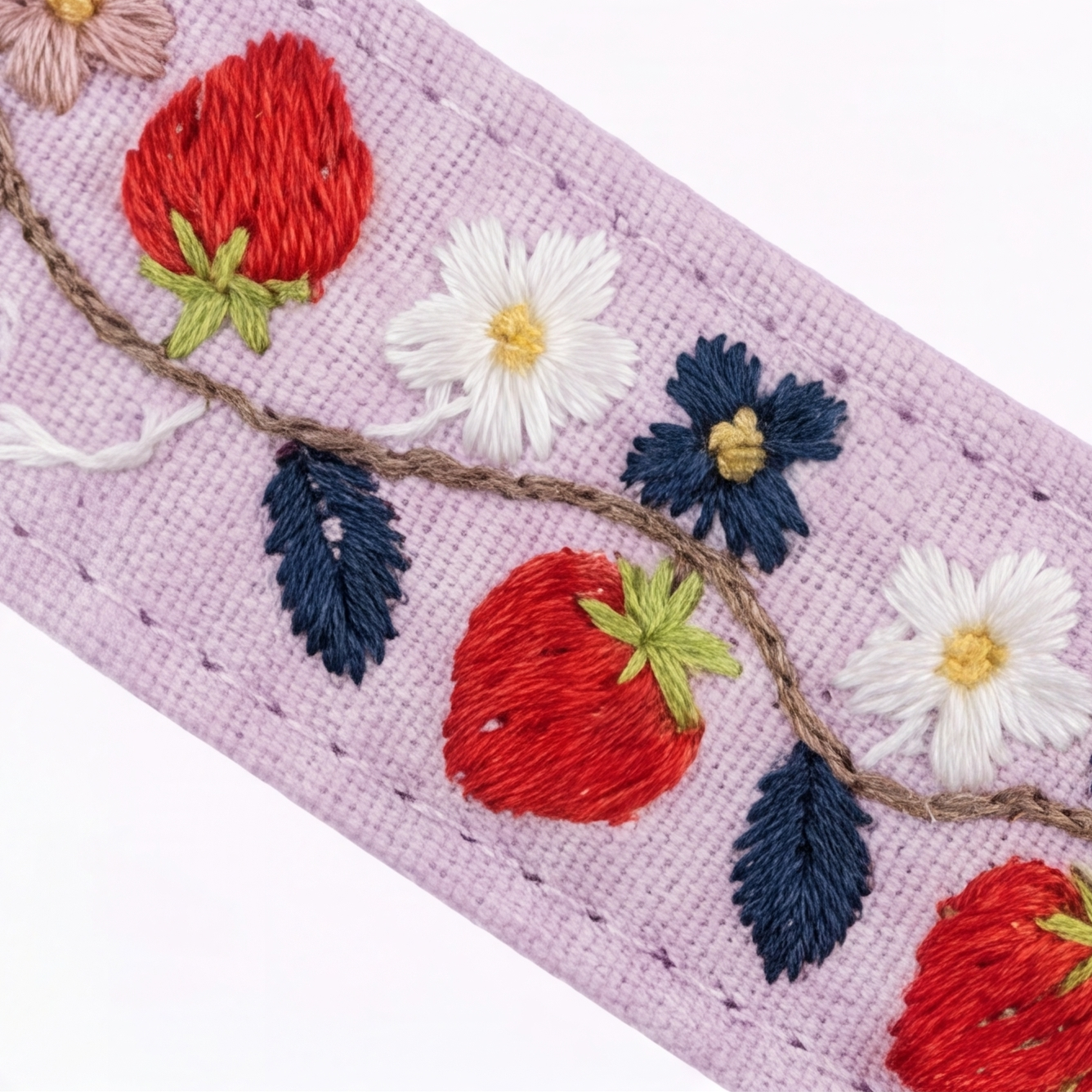 A close-up of a lavender embroidered fabric trim featuring red strawberries, white daisies, navy blue flowers, and dark blue leaves on a brown vine, set against a plain white background.