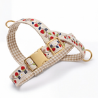 A dog collar with a beige and white gingham pattern, decorated with a red strawberry and blue flower floral print, and finished with gold-tone metal hardware.