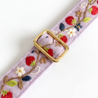 A lavender woven belt with embroidered strawberries, flowers, and leaves, featuring a gold-tone rectangular buckle, shown on a white background.
