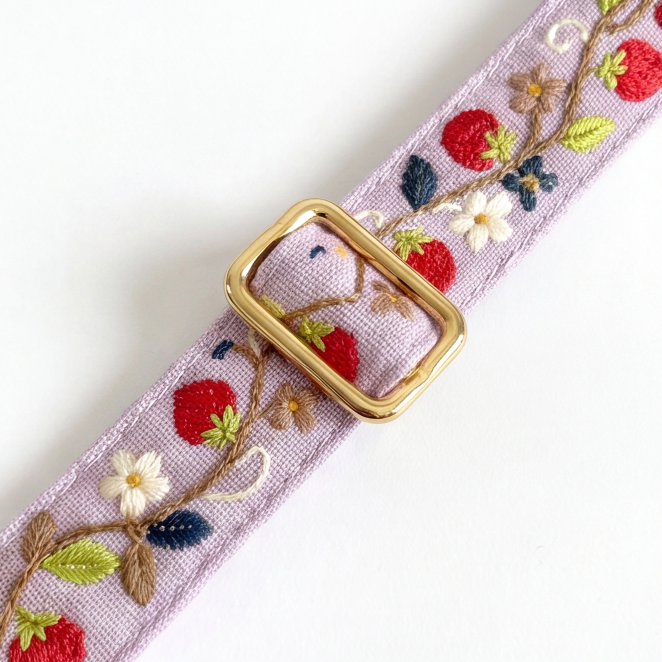A lavender woven belt with embroidered strawberries, flowers, and leaves, featuring a gold-tone rectangular buckle, shown on a white background.