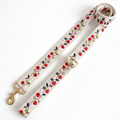 A woven leash strap with a floral and berry pattern, featuring a gold-tone swivel clasp and buckle, laid out on a white background.