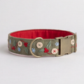 An olive green fabric dog collar with embroidered holly leaves, red berries, and small blue flowers, featuring a red interior lining and a brass-tone buckle.