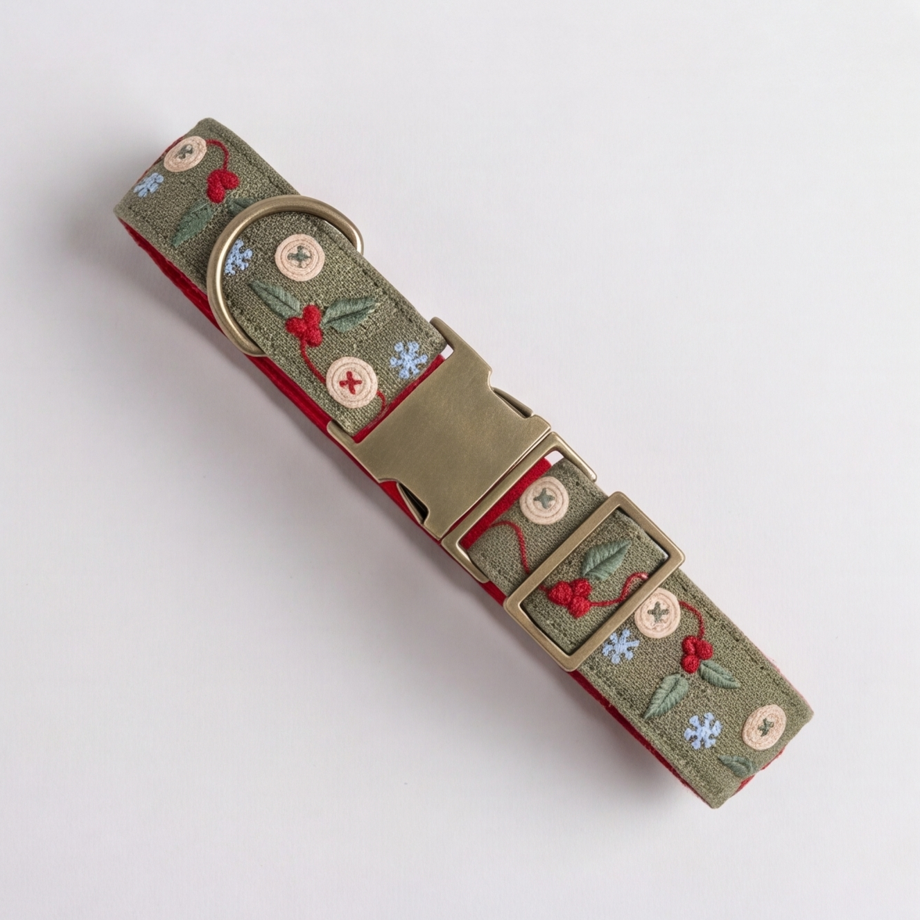 A dog collar with an olive green embroidered fabric featuring red berries, green leaves, and small blue and white flowers, complete with a brass buckle and D-ring, shown on a light gray background.