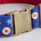 Close-up of a blue woven dog collar with embroidered holiday motifs and a brushed brass buckle.