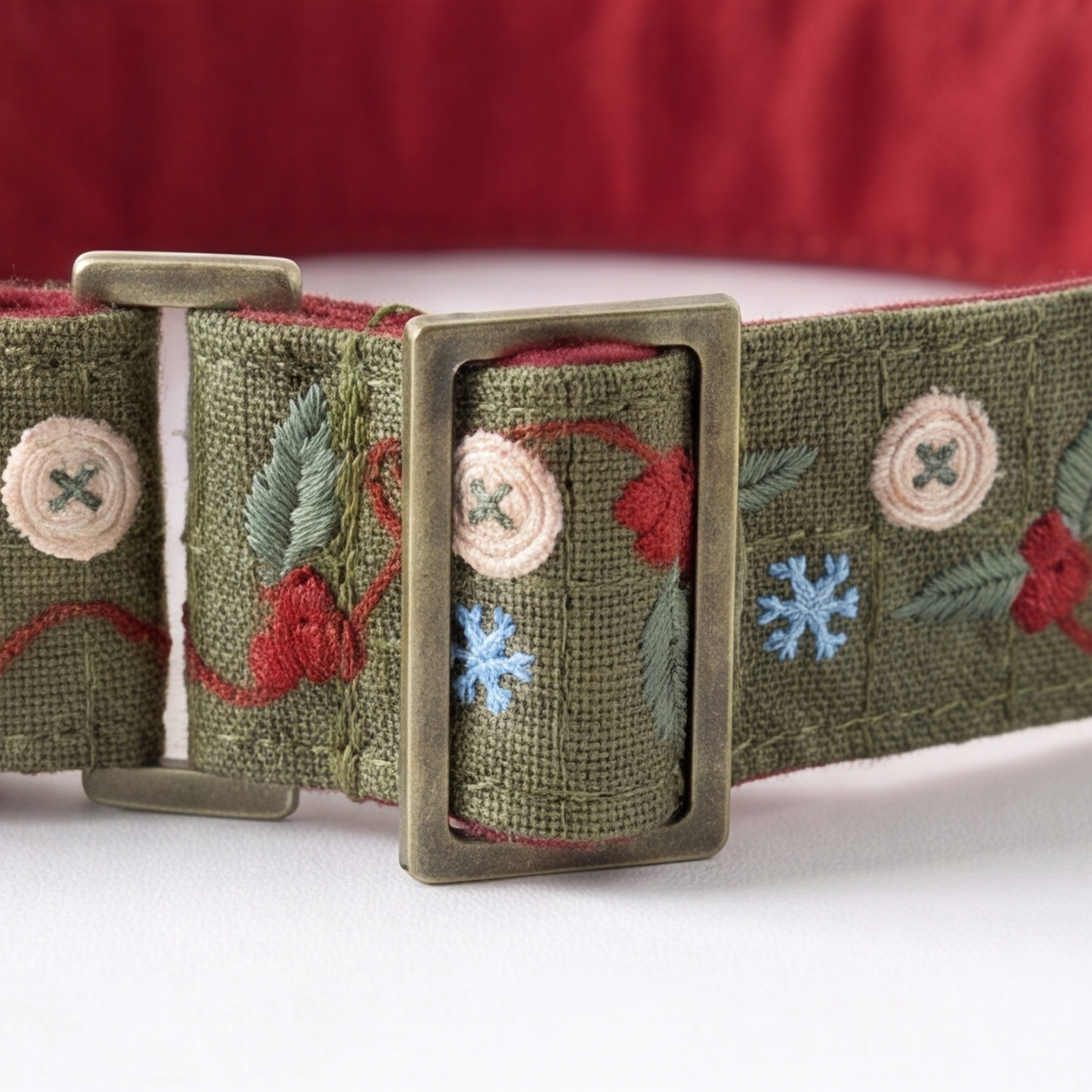 An olive green woven dog collar with embroidered red berries, green leaves, and snowflakes, featuring an antique bronze metal buckle.