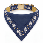 A navy blue triangular dog bandana with white floral embroidery and gold star accents, featuring a gold-tone metal buckle and a tan interior lining, shown on a white background.