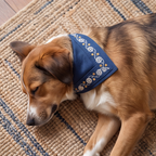 A brown and white dog lying on a woven rug, wearing a navy blue bandana with white snowflake embroidery and small gold star accents.