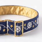 A close-up of a navy blue fabric collar with white embroidered snowflakes and gold embroidered stars, featuring a gold buckle and a shiny gold satin inner lining.