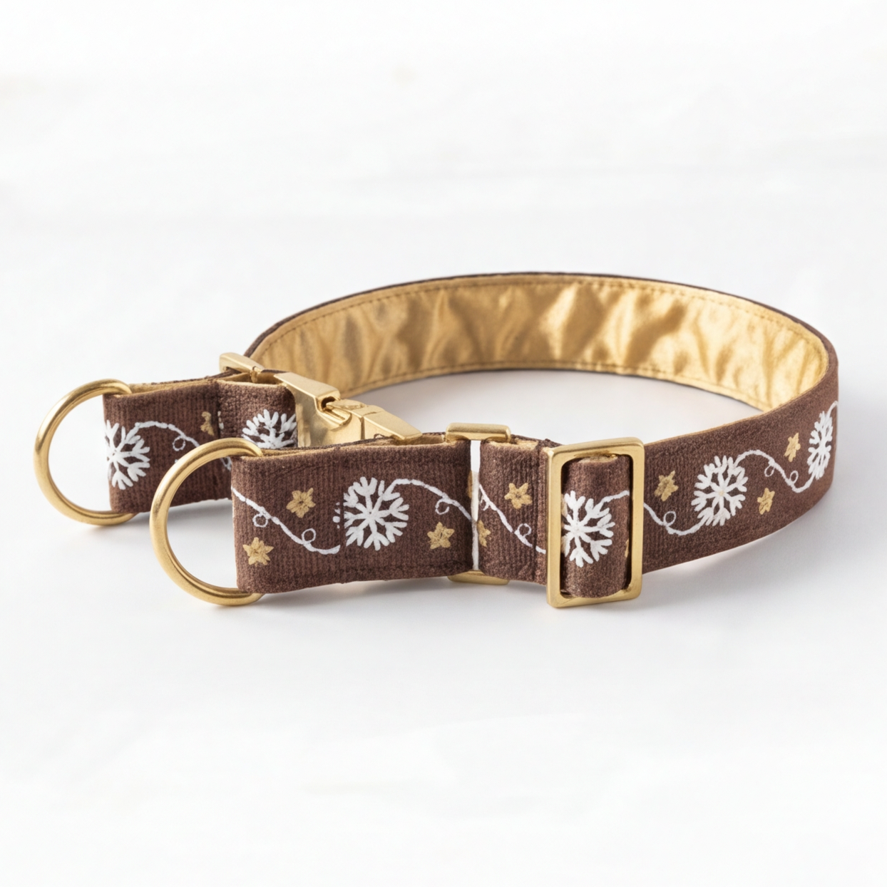 A brown fabric dog collar with a gold satin lining, decorated with white floral snowflake patterns and small gold stars, featuring gold-tone hardware.