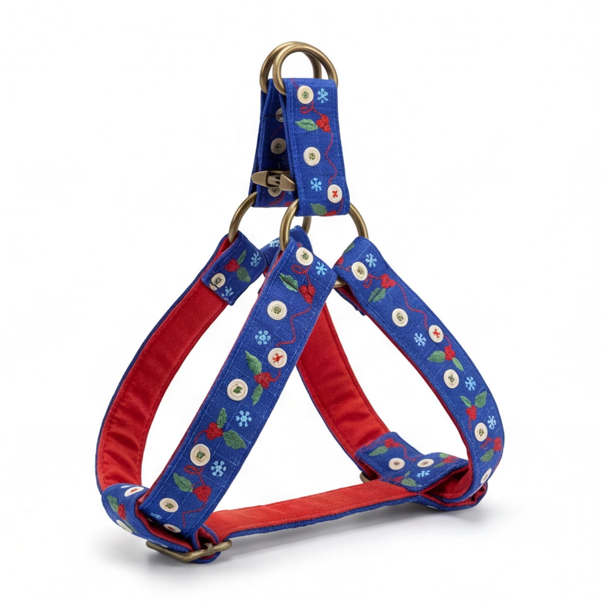 A blue dog harness with a festive embroidered pattern of white snowflakes, red berries, and green leaves, featuring a red interior lining and gold-tone metal hardware.