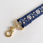 A close-up of a navy blue fabric strap with white floral embroidery and gold-tone metal hardware, including a lobster clasp, on a plain light background.