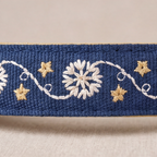 A close-up of a navy blue woven fabric trim or ribbon featuring white floral and vine embroidery with small gold star accents, shown against a neutral beige background.