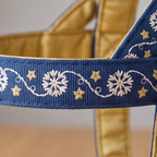 Close-up of a blue woven strap with white floral embroidery and small gold star accents, draped over a gold satin bag or pouch.