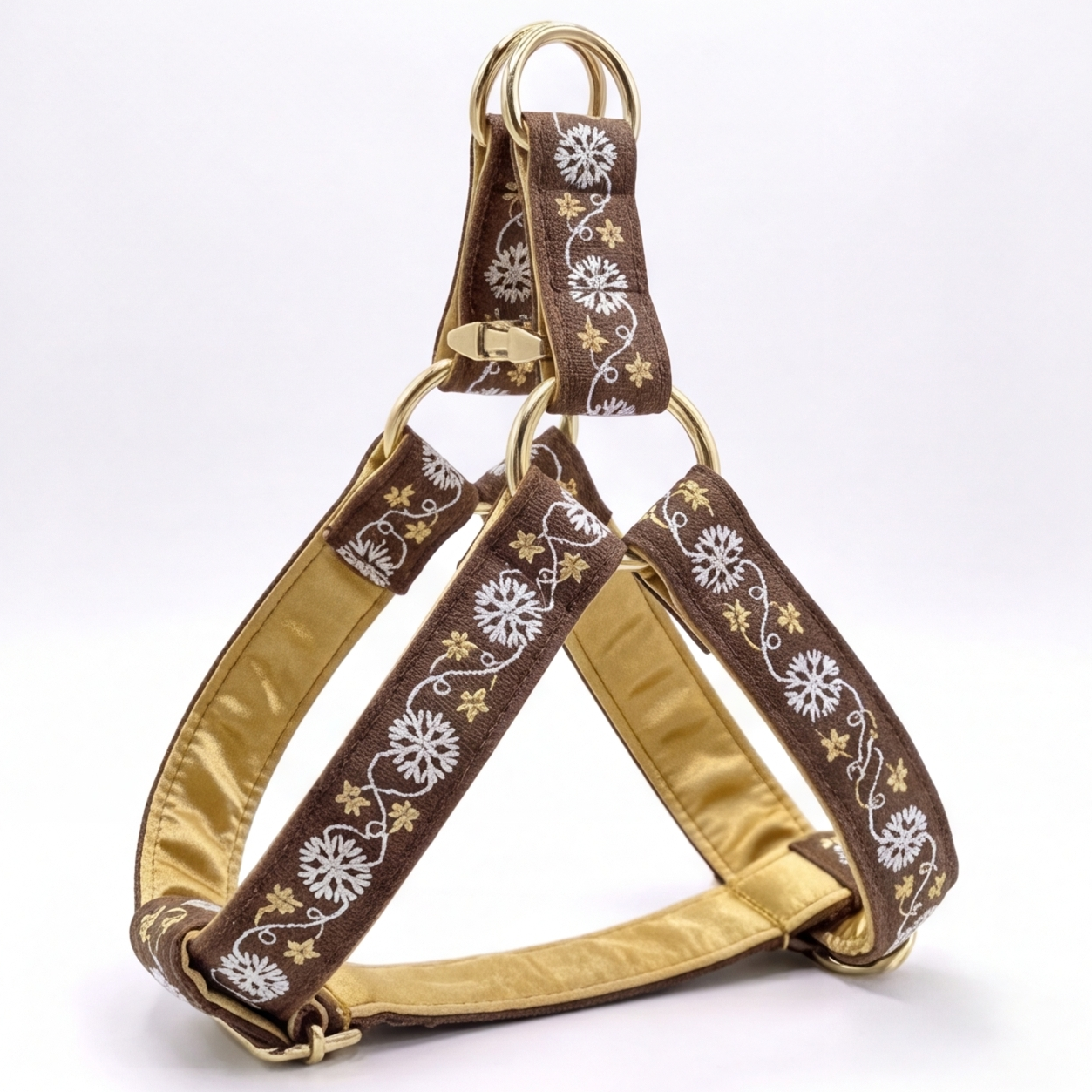 A brown and gold dog harness with white floral embroidery, featuring a gold satin lining and gold metal hardware, shown on a white background.