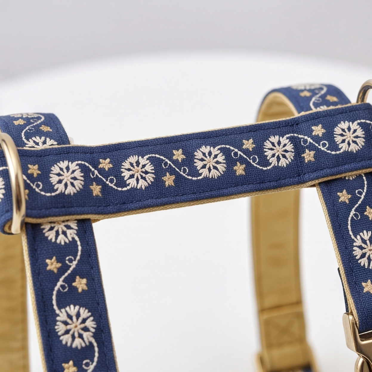 A close-up of a navy blue pet harness with white embroidered floral and star patterns, featuring gold-toned metal rings and a tan interior lining.