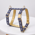 A blue and gold dog harness with a floral pattern, displayed on a white round table against a light gray background.
