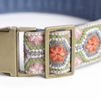 Close-up of a woven fabric belt with a brass buckle, featuring a geometric pattern in blue, green, white, and pink with orange floral accents.
