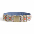 A patterned fabric dog collar with a blue interior, featuring a pink, green, and white geometric design with orange floral motifs, and a gold-tone metal buckle and D-ring, shown on a white background.