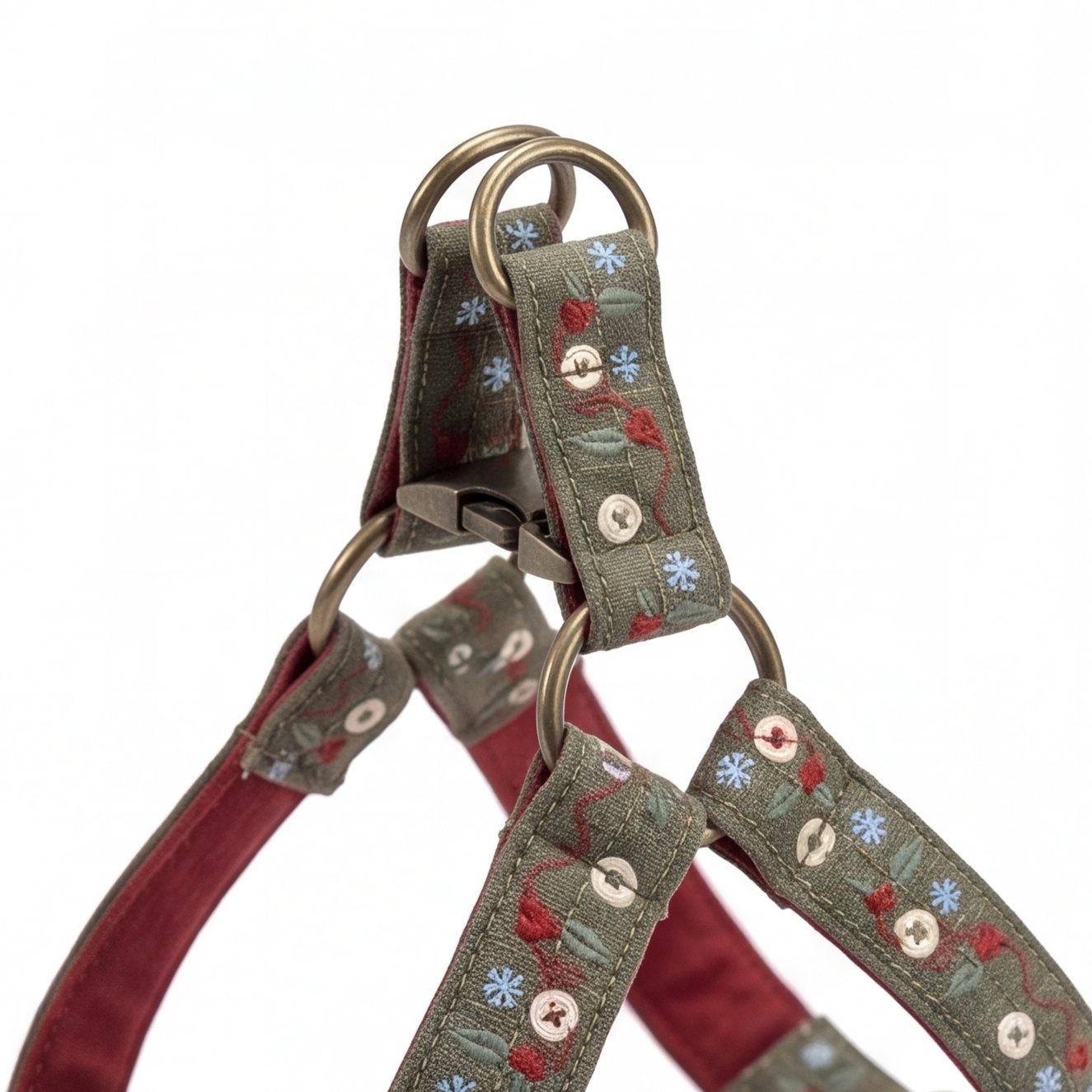 A close-up of a dog harness strap featuring olive green fabric with embroidered red and blue floral details, metal rings, and a burgundy inner lining, shown against a plain white background.