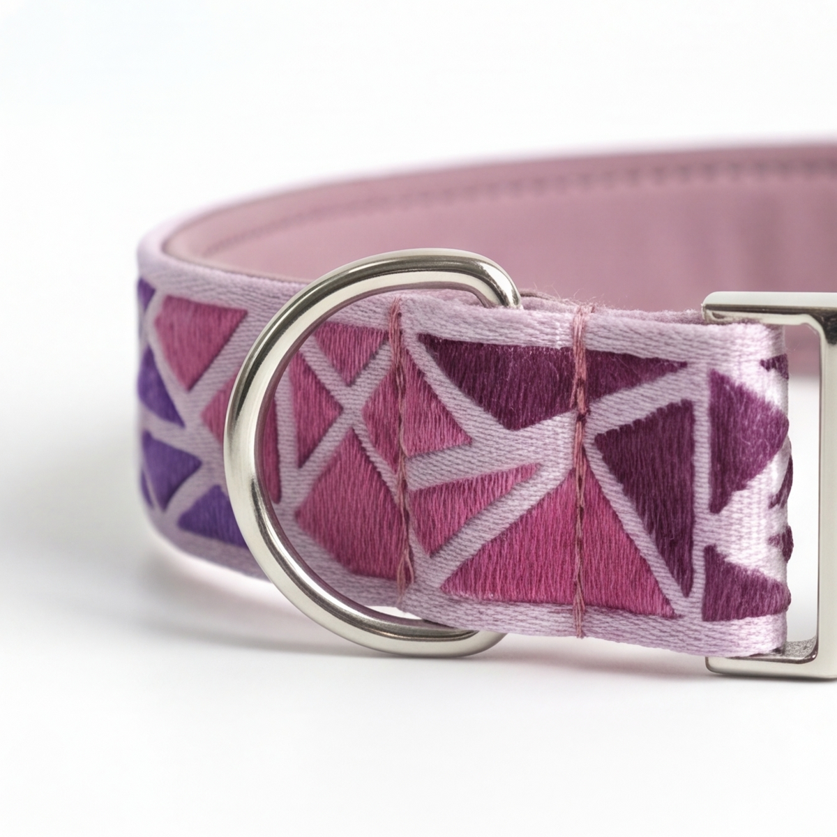 A close-up of a pink and purple patterned fabric collar with a silver metal D-ring and buckle, shown on a white background.
