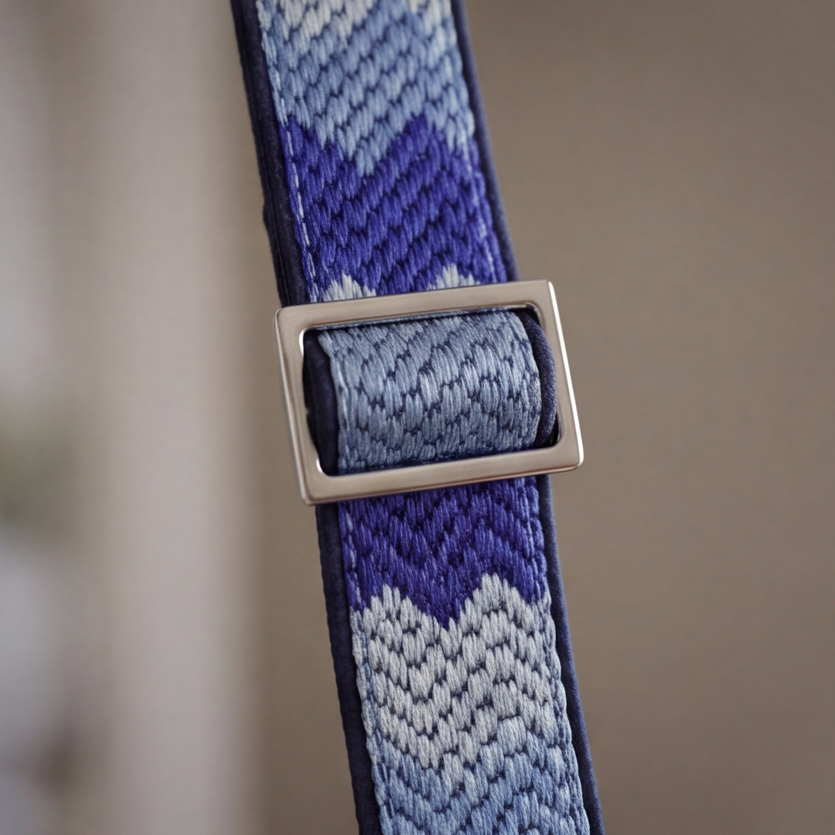 A close-up of a woven strap with a geometric chevron pattern in shades of blue, purple, and white, featuring a silver-toned metal buckle.
