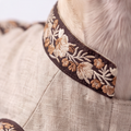 Close-up of a beige textured pet coat or jacket with a wide embroidered collar trim in brown, cream, and tan floral embroidery, shown on a light cream-colored dog.
